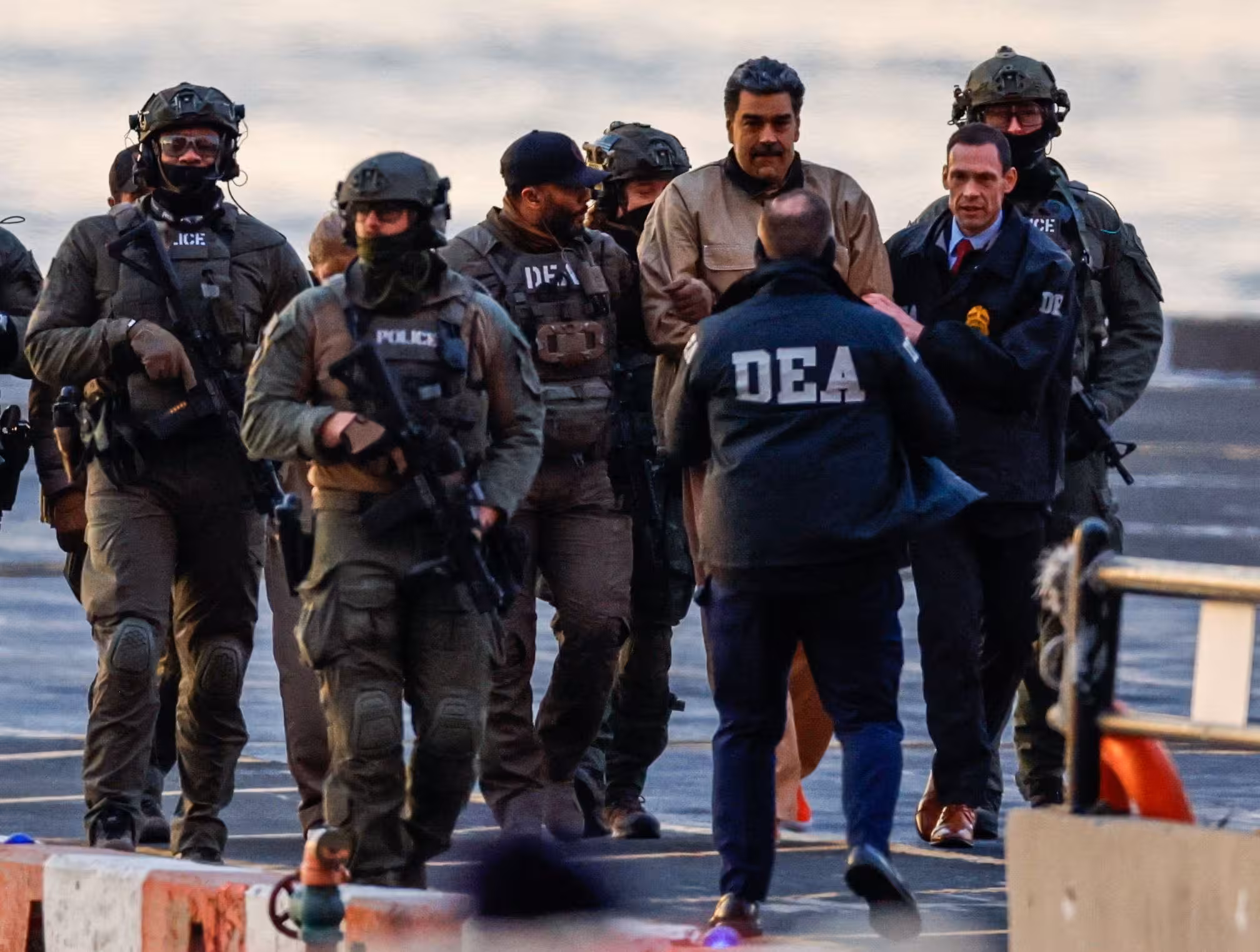 Operativo de fuerzas de seguridad de Estados Unidos con agentes armados y personal de la DEA escoltando a Nicolás Maduro en una pista de aterrizaje, con chalecos tácticos, cascos y equipo policial visible.