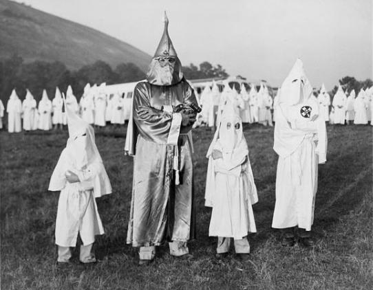 Dos niños vestidos con túnicas y capuchas del Ku Klux Klan están a ambos lados del Dr. Samuel Green, Gran Dragón del Ku Klux Klan, en una ceremonia de iniciación en Atlanta, Georgia. 24 de julio de 1948.